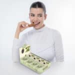 אישה צעירה נאה מחייכת ונוגסת בחטיף בריאות. לפניה מופיע מארז של 16 חטיפי בריאות מבית the123