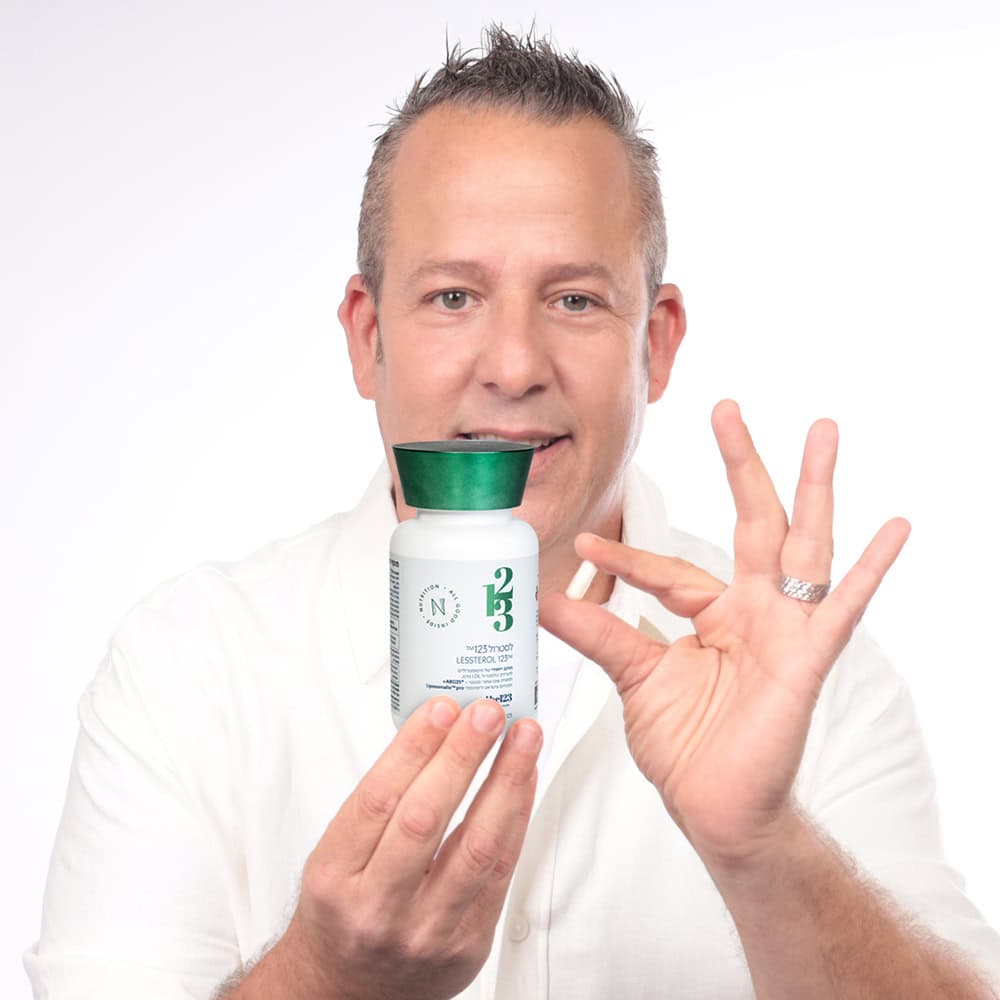 גבר בגיל ביניים מחייך למצלמה, כאשר הוא מחזיק ביד אחת בקבוק של תוסף תזונה לסטרול 123™ | 123 קפסולות ובידו השנייה הוא מחזיק קפסולה בודדת.